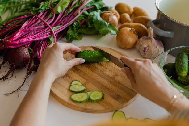 从肩膀上看，厨房里女性用刀在木板上切黄瓜。健康饮食。图片下载