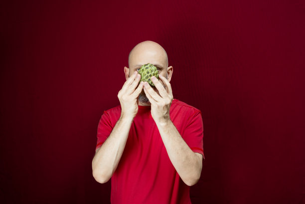 年轻英俊的男子，光头，红衬衫，手持松果站在红色的背景。图片下载