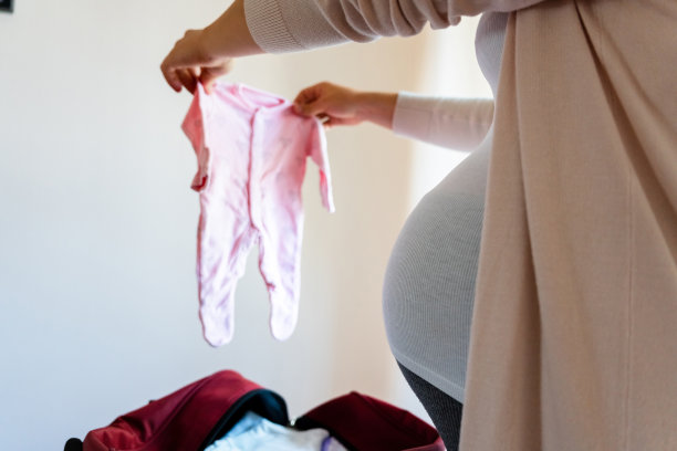 孕妇婴儿衣服。漂亮的怀孕妈妈穿着黄色的婴儿服。孕妇抱着肚子，打包产科包。概念产妇，怀孕，分娩。图片下载