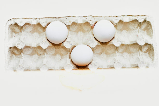 三个白鸡蛋放在白色背景的硬纸盘里。图片下载