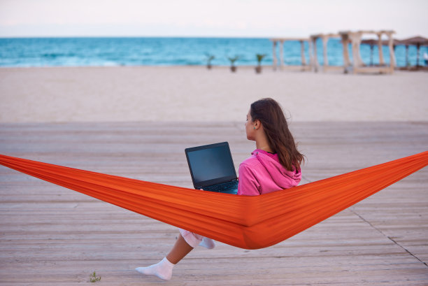 年轻女子坐在吊床上，在海边的笔记本电脑上远程工作图片下载