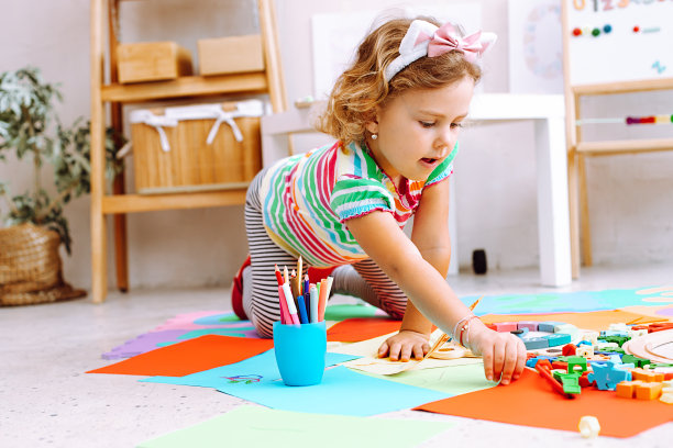 肖像集中的小女孩站在四个红色的纸周围彩色的纸，房间里的玩具。图片下载