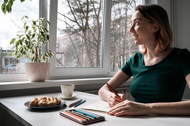 穿着绿色t恤的年轻女子坐在桌子旁用铅笔画画。图片下载