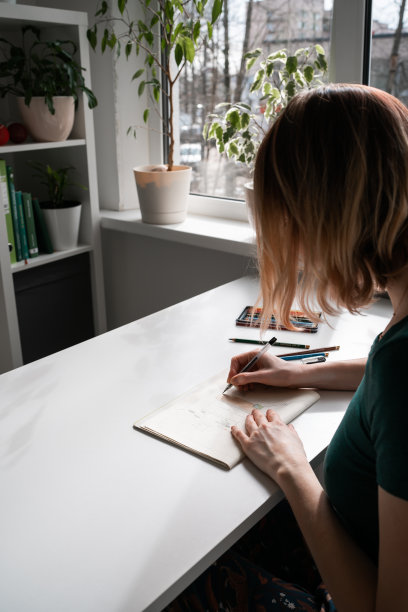 年轻女子坐在窗边画画。图片下载
