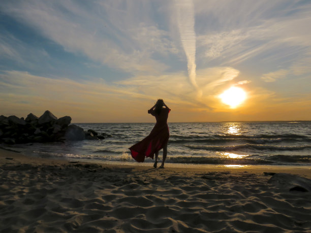 一个迷人的女人在海边穿着红色的裙子，背景是日落时的波浪图片下载