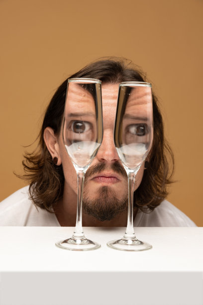 透过酒杯看到幸福男人的脸。物体变形，光学错觉。简约的当代艺术。图片下载