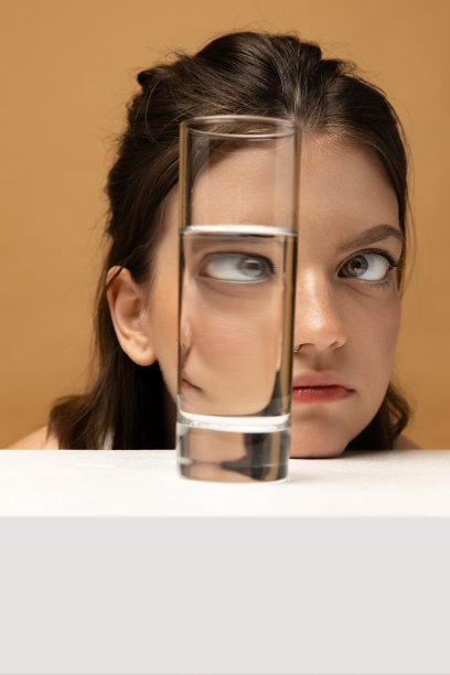 当代艺术肖像的漂亮女孩看着玻璃水。物体变形，光学错觉。艺术概念，创意，超现实主义图片下载