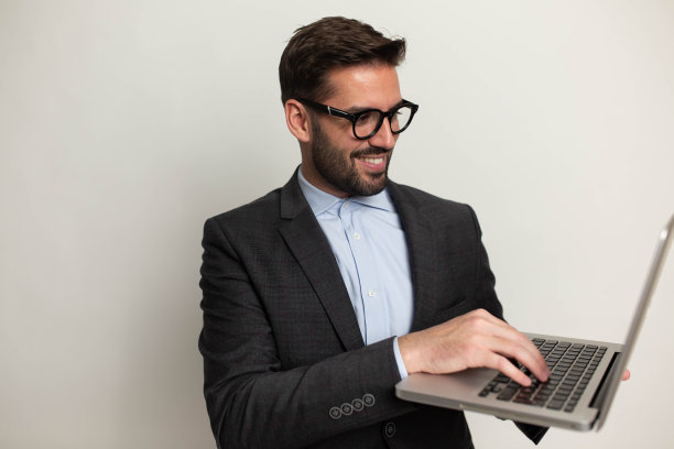 穿着西装戴眼镜的商人拿着笔记本电脑，白色背景的工作室肖像图片下载