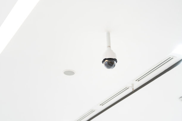 白色闭路电视监控挂在通风口旁边的白色天花板上。图片下载