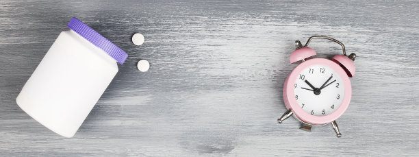 女性健康的概念。医药、保健风格。副本的空间。蓝色木头背景的白色塑料瓶上有药片和时钟。横幅图片下载