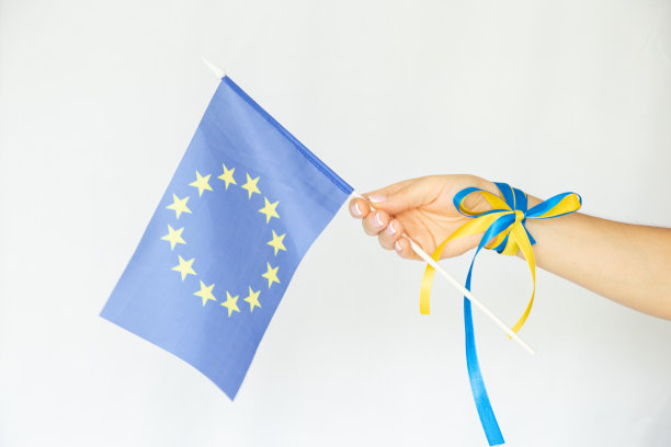 一名女性手举着白色背景的欧盟国旗，打着黄蓝蝴蝶结，象征友谊图片下载