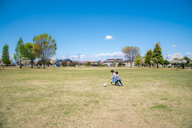 日本儿童在蓝天下的公园里踢足球图片下载