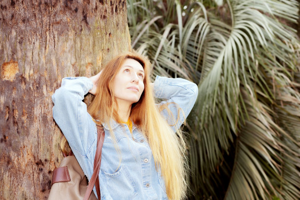 一个女人倚在棕榈树干上。一个女人站在一棵棕榈树的树干旁图片下载