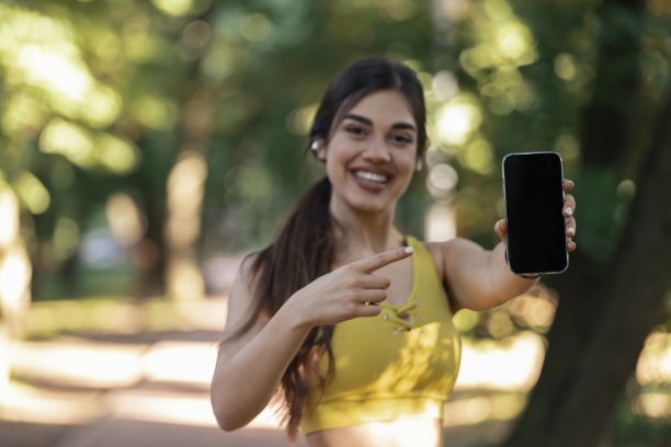 戴着耳机的漂亮女孩正拿着手机指着它。图片下载