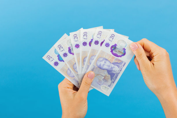 图片是一个女人的手，她的手拿着英镑，孤立在蓝色的工作室背景。图片下载