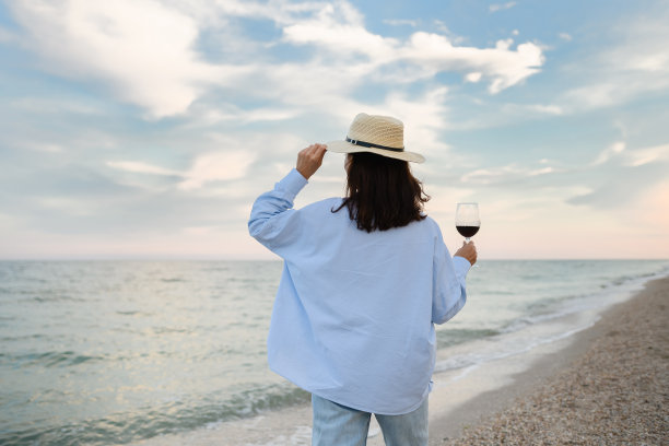 年轻女子拿着一杯红酒，背景是大海。图片下载