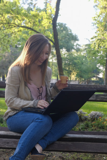 年轻女子在公园里一边喝咖啡，一边用笔记本电脑工作图片下载