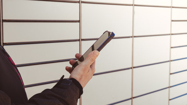 女性手拿手机，旁边的包裹柜从购物柜收集包裹。女性Skans二维码在手机上自助寄存柜单元与条码阅读器现代运输和递送非接触式自动化邮筒图片下载