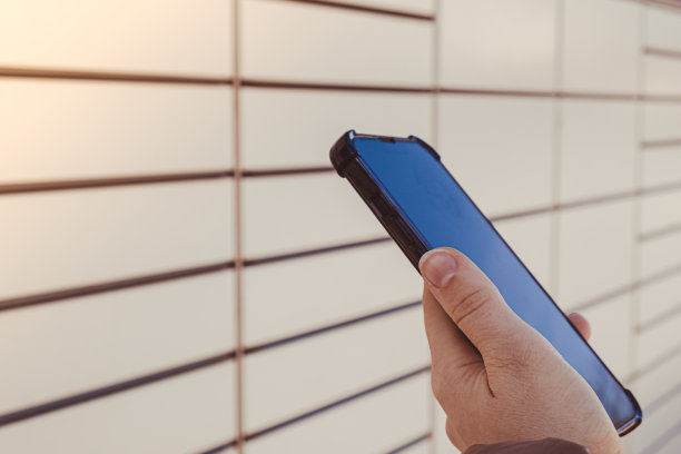 女性手拿手机，旁边的包裹柜从购物柜收集包裹。女性Skans二维码在手机上自助寄存柜单元与条码阅读器现代运输和递送非接触式自动化邮筒图片下载