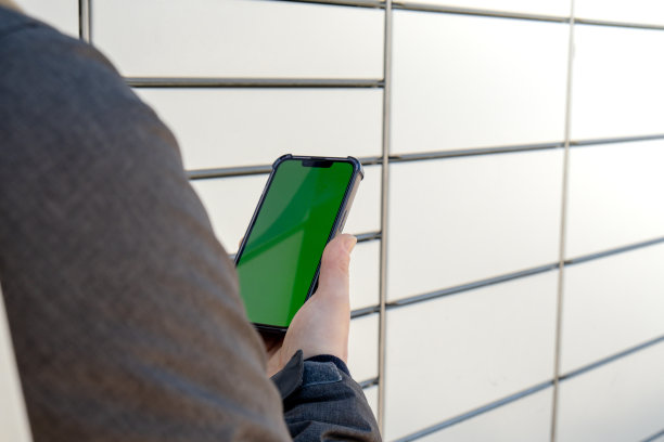 女性手持手机与绿色屏幕色度键旁边的包裹柜收集包裹从购物柜。女子在手机自助服务上扫二维码图片下载