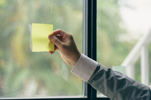 年轻的商人手里拿着一张便利贴，彩纸贴在玻璃墙上图片下载