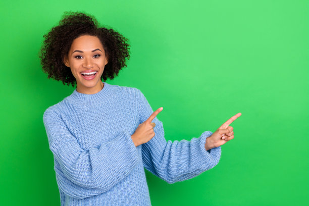 漂亮的喜气洋洋的女孩的肖像与卷发穿蓝色oversize套衫指示空白孤立在绿色背景色图片下载