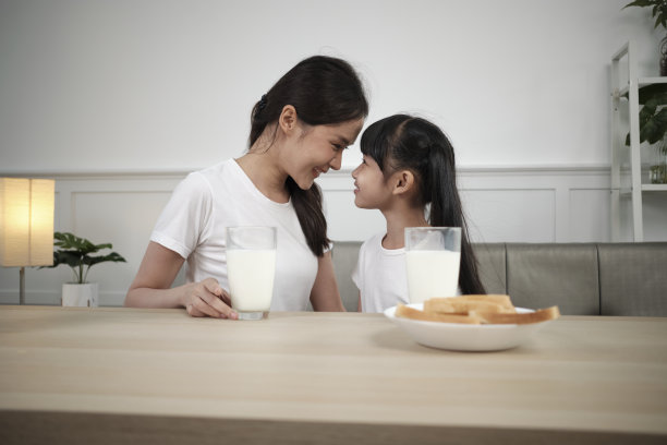 健康的亚洲妈妈和女儿一起在餐桌上喝鲜奶。图片下载