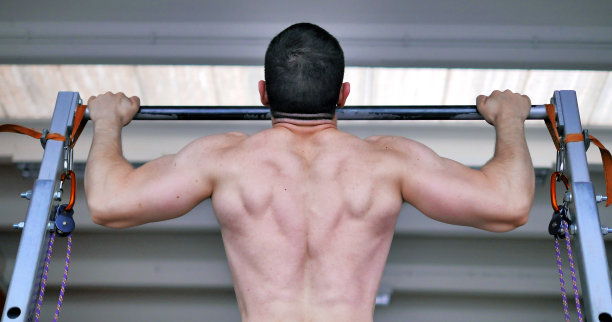 肩宽背宽的健美运动员用杠铃做引体向上。图片下载