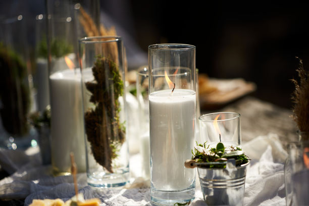 婚礼宴会在户外森林。餐桌上装饰着波西米亚风格的蜡烛，白布，鲜花，用盘子，餐具，盘子，饭菜，高脚器皿和饮料。节日餐饮。图片下载