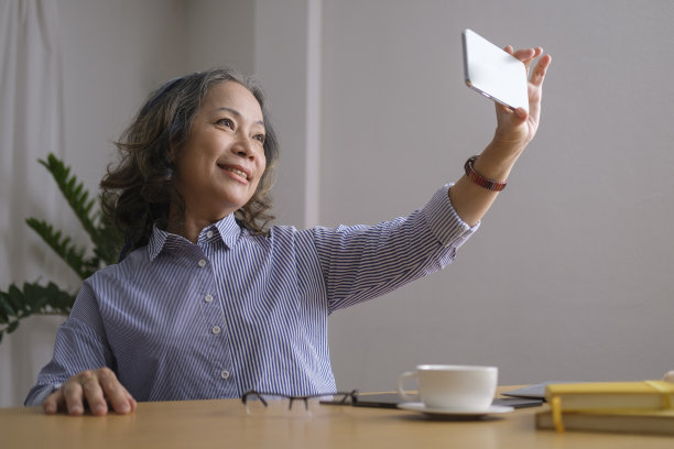 快乐的中年女性用手机自拍，花时间在客厅的科技设备。图片下载