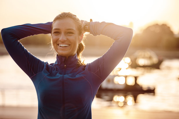 穿着运动服微笑的年轻女子在夕阳下的河边图片下载
