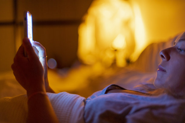 女人晚上在床上看手机。图片下载