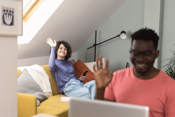 年轻的非洲裔男子在网上工作，他的女朋友在沙发上用智能手机图片下载