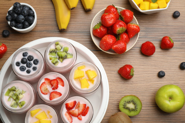 酸奶机与罐子和不同的水果，在木制桌子上，平铺图片下载