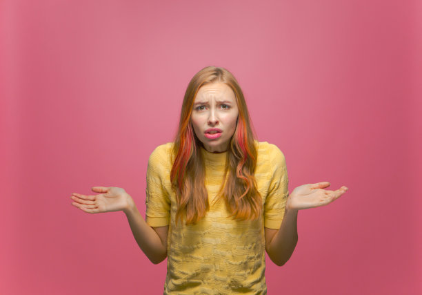 困惑不满的年轻女孩摊开双手在问什么，皱着眉头，误解在粉红色的工作室背景上图片下载