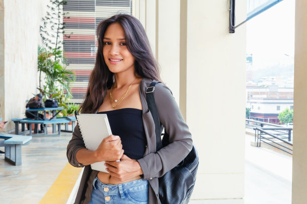 拉丁裔少女，学生微笑相机与笔记本和书包图片下载