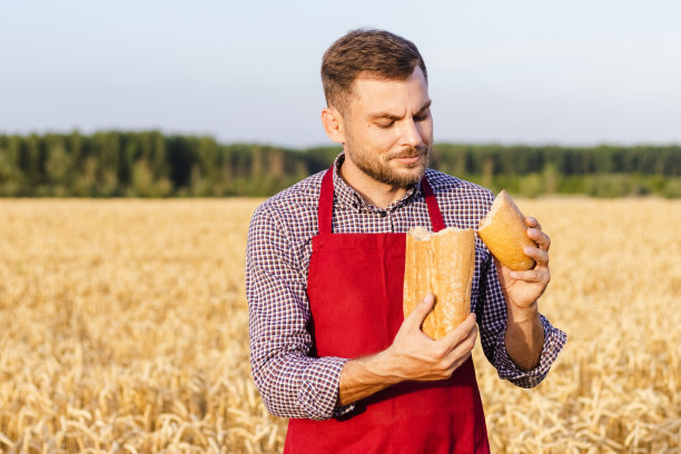 年轻的成年男子农民面包师检查面包的质量和微笑，而站在麦田。图片下载