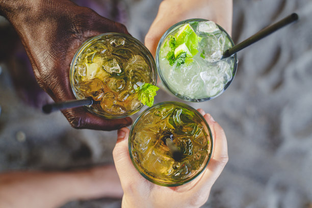 多民族的人在沙滩上拿着一杯新鲜的莫吉托鸡尾酒的特写，背景是沙子图片下载