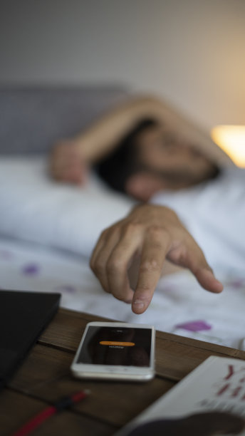 昏昏欲睡的年轻人在床上继续睡觉时关掉了闹钟图片下载