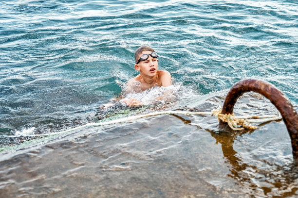 一名男孩抱着绳子在水中游泳，试图爬上码头图片下载