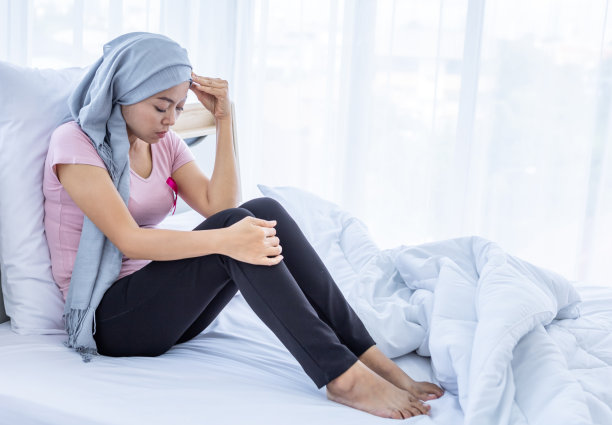 一名亚洲女性疾病乳腺癌患者头痛贴粉色丝带戴头巾化疗治疗后坐在床上在家里的卧室，保健，药物图片下载