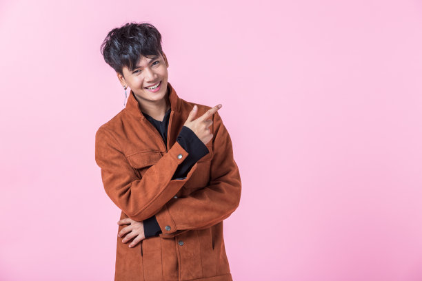 亚洲的一个男人英俊的年轻用两只手和手指指着一边的眼睛看着相机在爱孤立的粉红色空白拷贝空间工作室的背景。图片下载