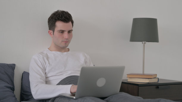 男人在床上用笔记本电脑工作图片下载