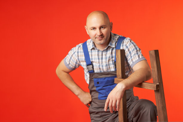 一个穿着工作服的秃头男子正微笑着一只手靠在木梯上图片下载