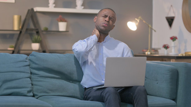 非洲男子坐在沙发上用笔记本电脑脖子疼图片下载