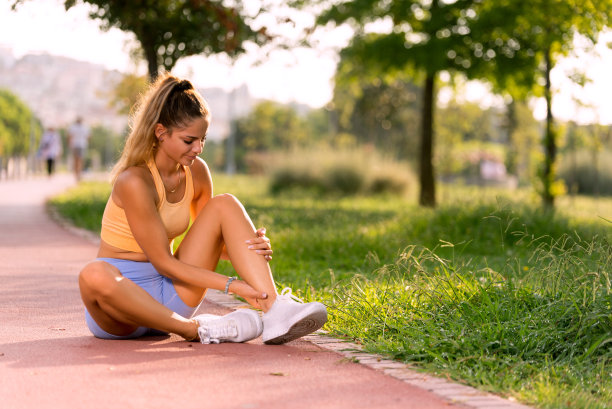 20多岁的女性穿着黄色上衣和蓝色紧身衣，在跑道上痛苦地抱着脚踝的照片图片下载