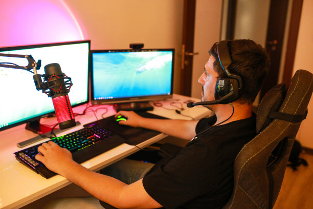 年轻男性晚上坐在桌边玩电脑游戏和直播。图片下载