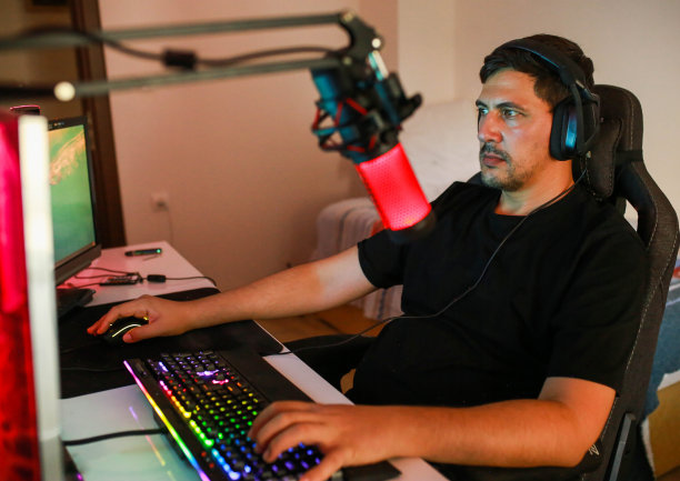 年轻男性晚上坐在桌边玩电脑游戏和直播。图片下载