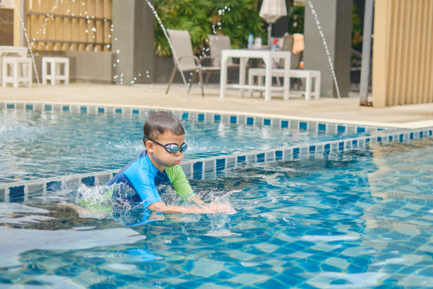 亚洲小朋友夏天戴着泳镜，穿着泳装，在户外泳池学习游泳图片下载