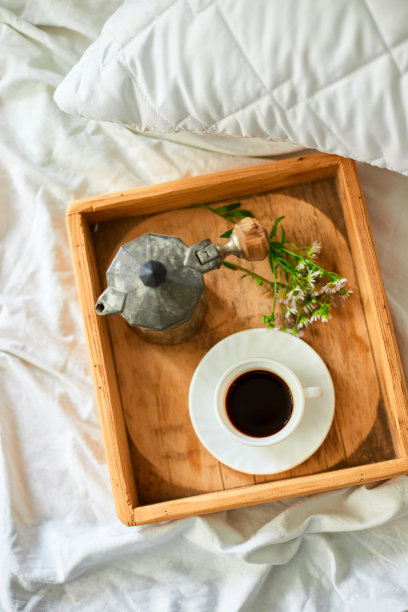 咖啡杯，间歇泉咖啡机和白色床单上的托盘上的花，早上好，酒店房间清晨，早餐在床上图片下载